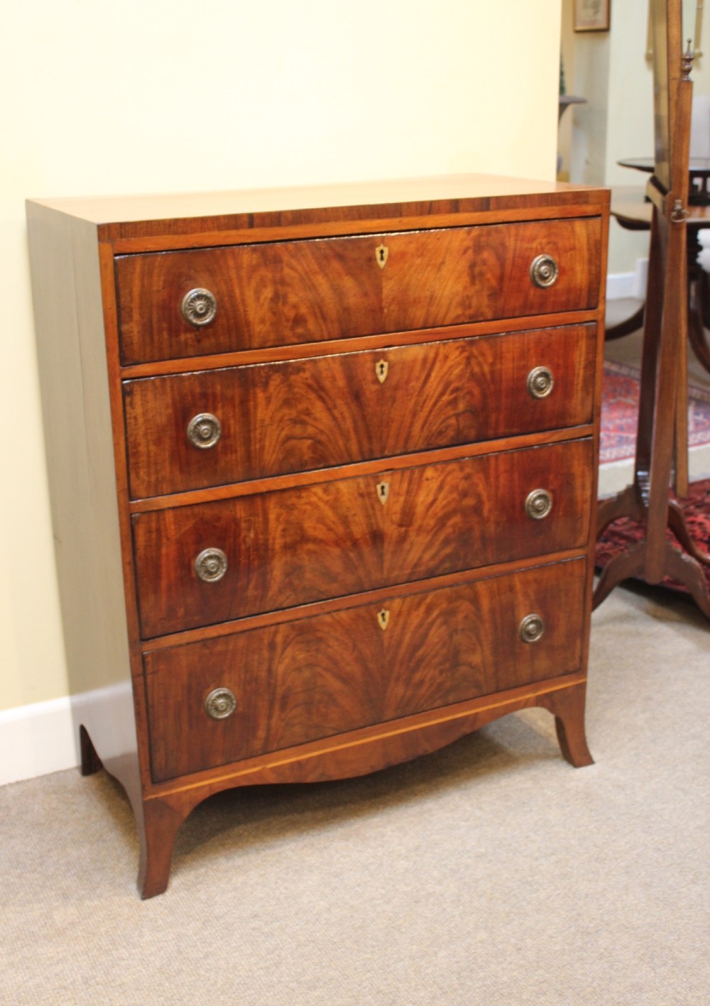 A nineteenth-century mahogany chest of four graduated drawers featuring flame mahogany grain and brass handles. View VI