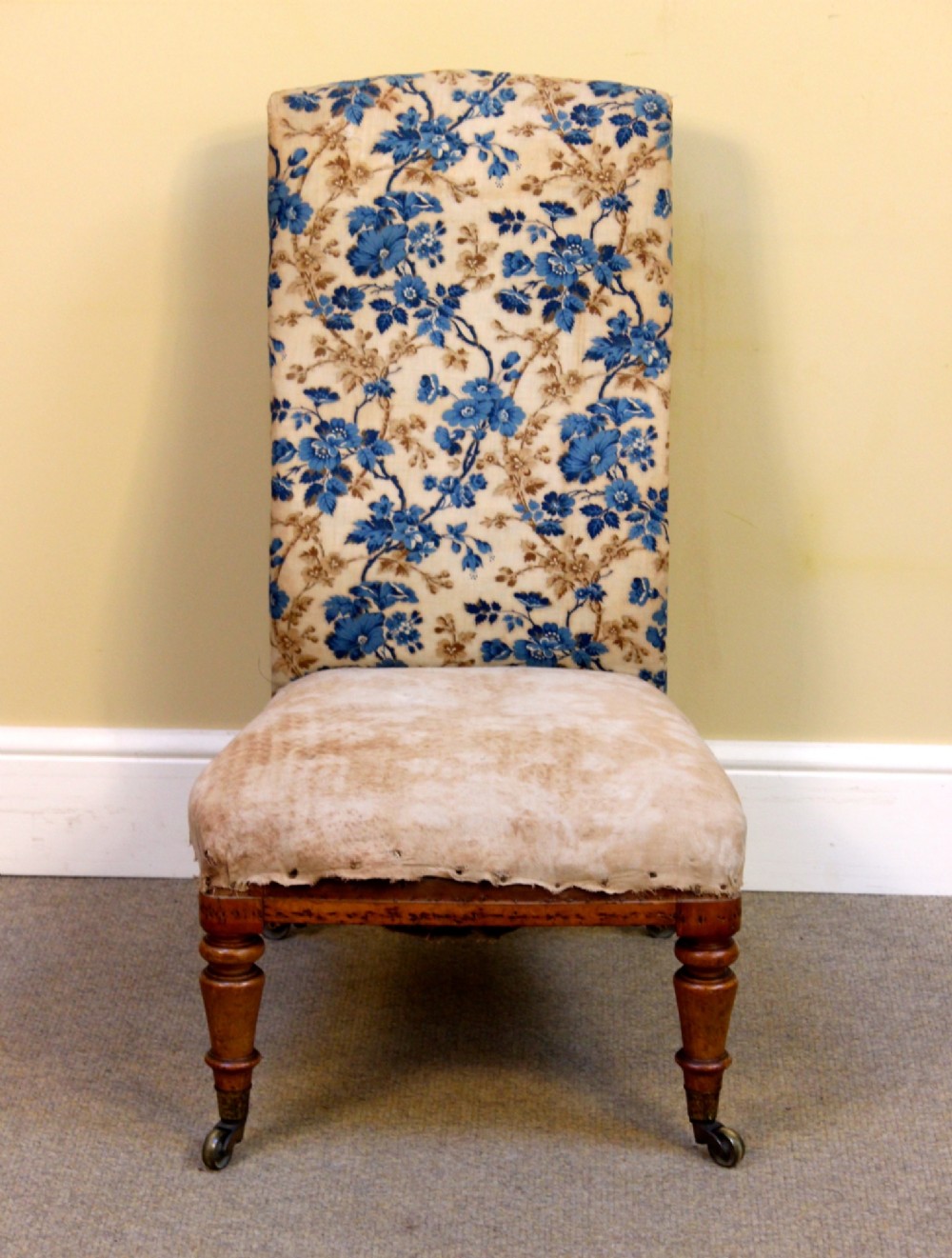 A 19th-century low-seated nursing chair with turned front legs on brass castors, a beige upholstered seat, and a curved backrest covered in blue floral fabric. View III