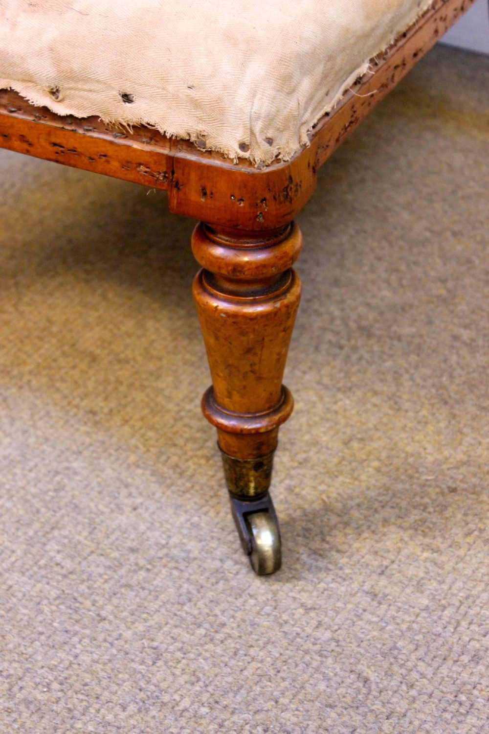 A 19th-century low-seated nursing chair with turned front legs on brass castors, a beige upholstered seat, and a curved backrest covered in blue floral fabric. View IV
