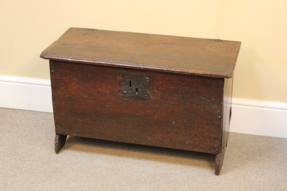 A 17th-century dark oak six-plank coffer featuring a hinged rectangular lid, hand-forged iron lockplate, and slab sides.
