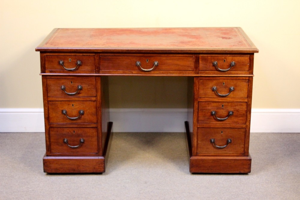 A 19th-century mahogany pedestal desk featuring an inset leather writing top, nine drawers with brass handles, and plinth bases.