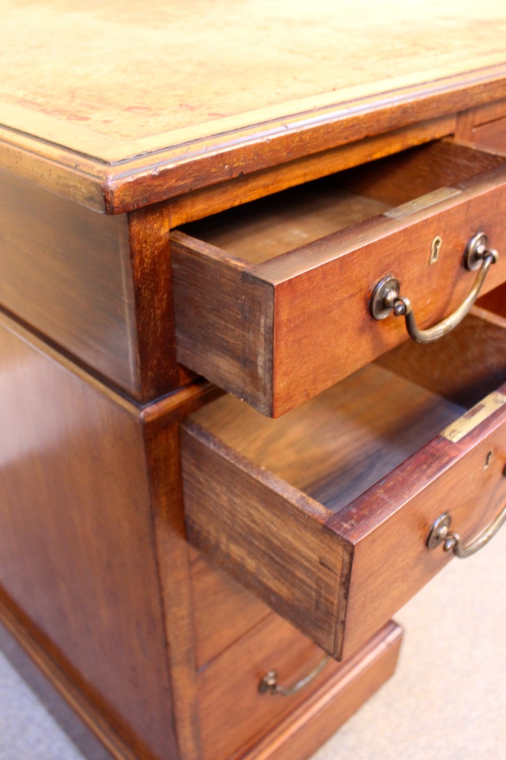 A 19th-century mahogany pedestal desk featuring an inset leather writing top, nine drawers with brass handles, and plinth bases. View V