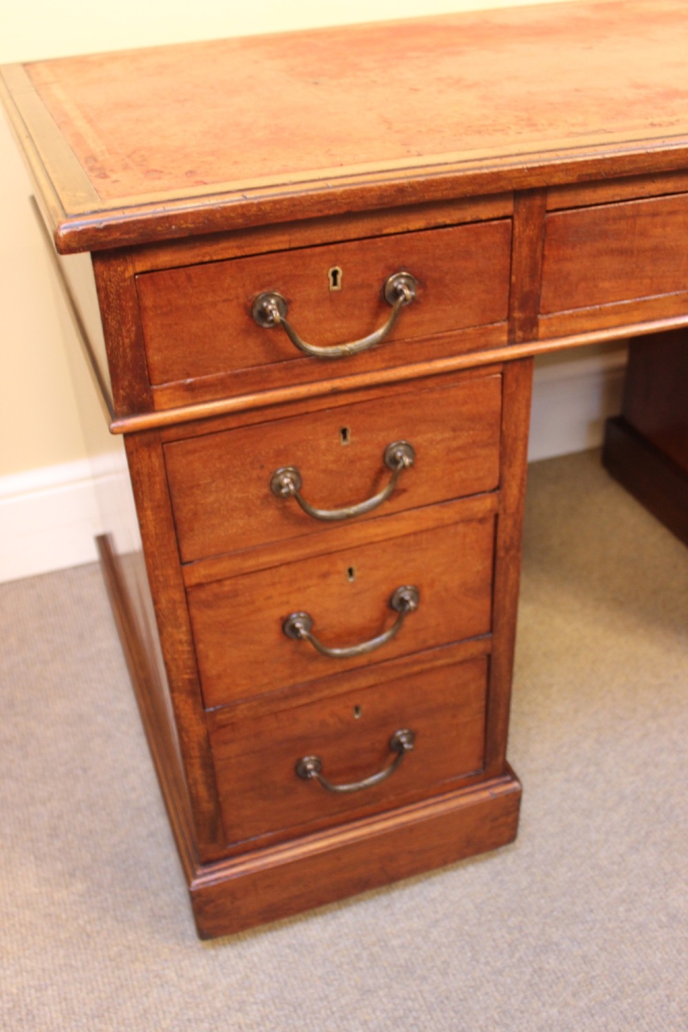 A 19th-century mahogany pedestal desk featuring an inset leather writing top, nine drawers with brass handles, and plinth bases. View VI
