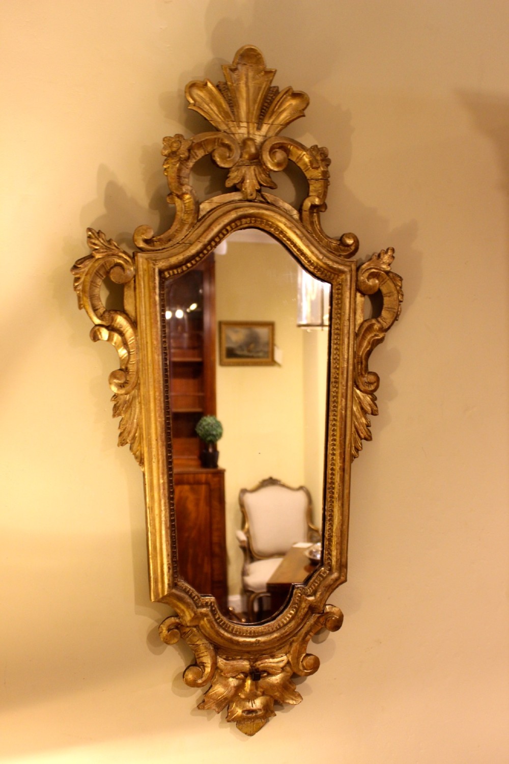 A nineteenth-century Rococo style gilded wall mirror featuring elaborate C-scroll carvings, a shell cresting, and a carved lower mask apron. View II