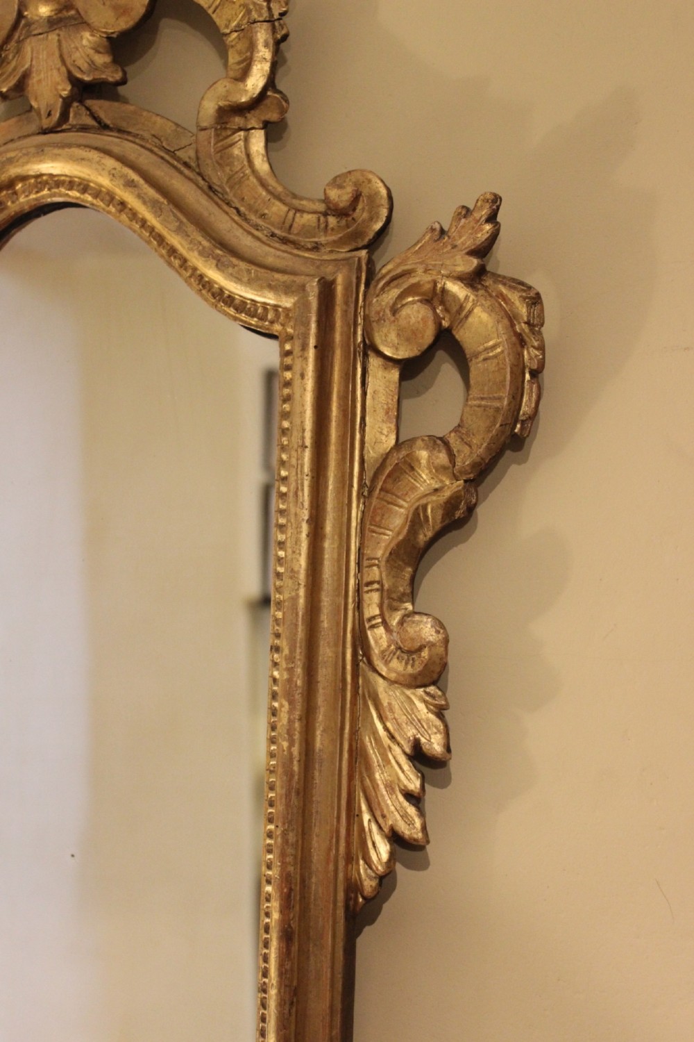 A nineteenth-century Rococo style gilded wall mirror featuring elaborate C-scroll carvings, a shell cresting, and a carved lower mask apron. View V