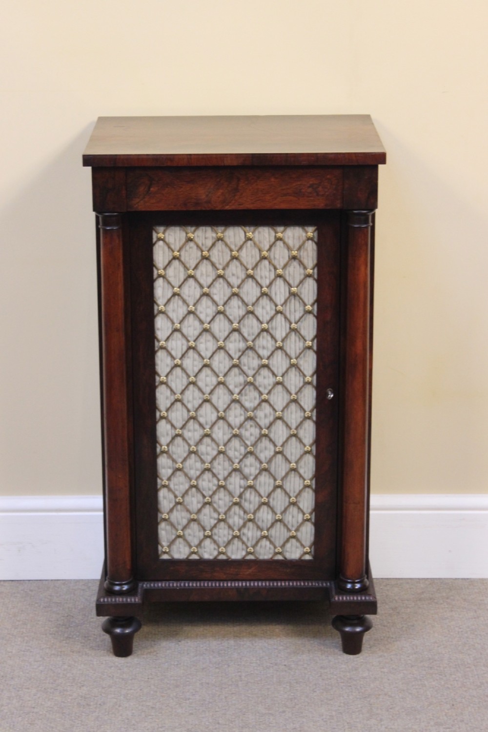 A 19th-century rosewood pier cabinet featuring a single door with a brass wire grille over pleated fabric, flanked by turned columns. View II