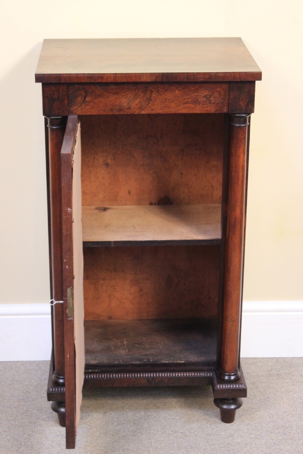 A 19th-century rosewood pier cabinet featuring a single door with a brass wire grille over pleated fabric, flanked by turned columns. View VI