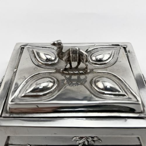 A square sterling silver trinket casket featuring a camel finial on the lid and detailed desert relief panels along the sides. View II