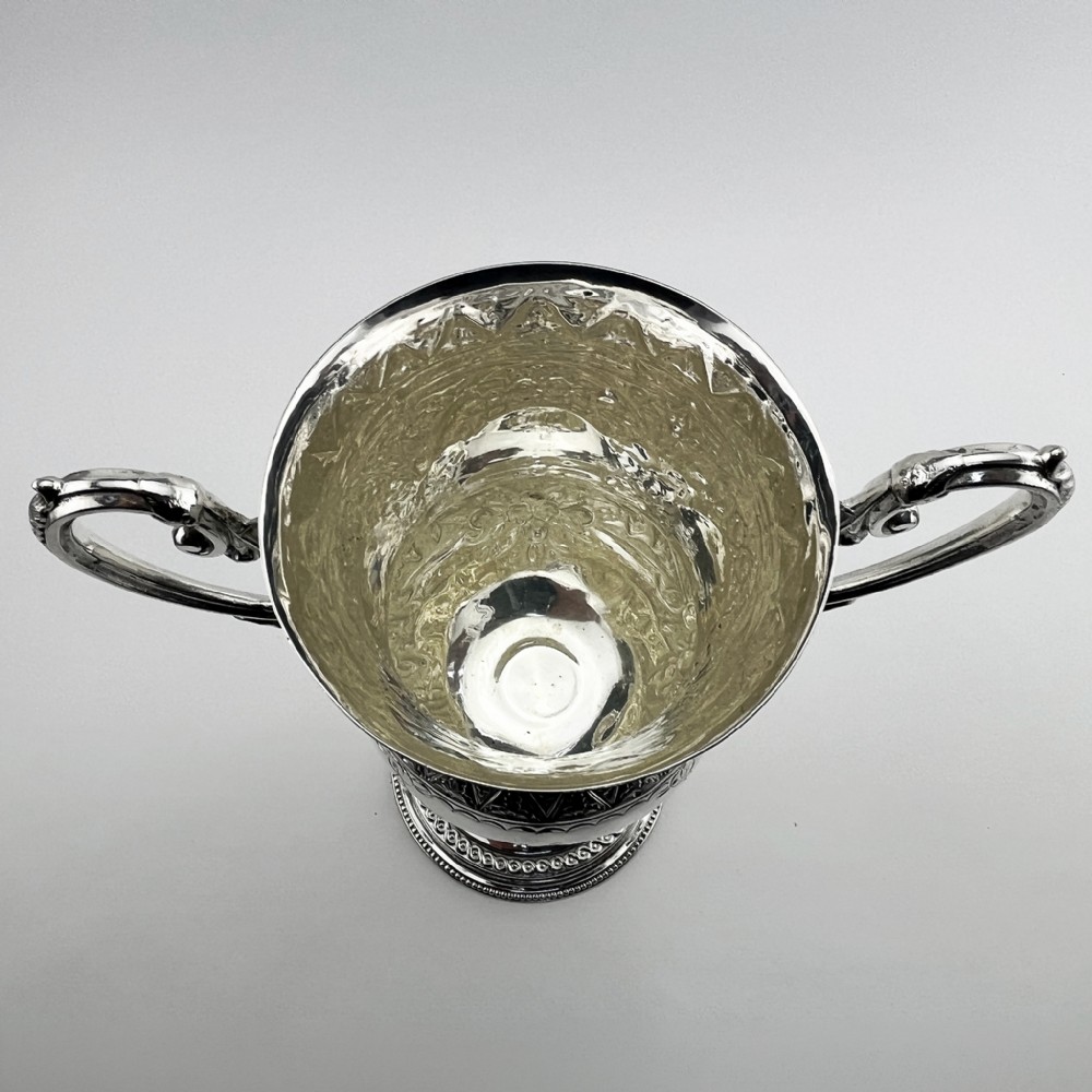 A Victorian silver plated trophy cup featuring ornate scrolled handles, repousse floral engraving, and a circular decorated pedestal foot. View IV