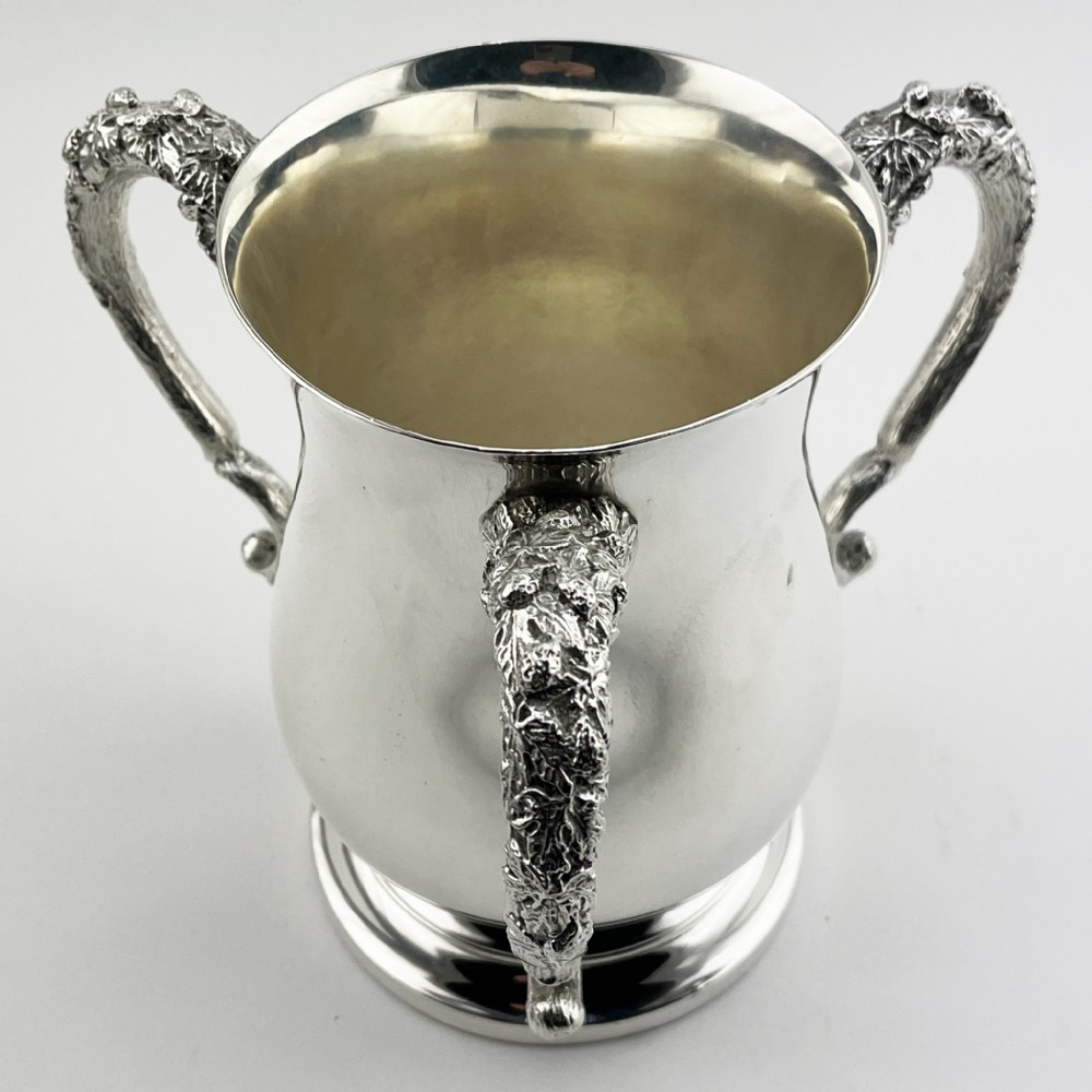 An Edwardian silver-plated loving cup featuring a polished bell-shaped body mounted with three ornate cast handles decorated with vine leaf motifs.