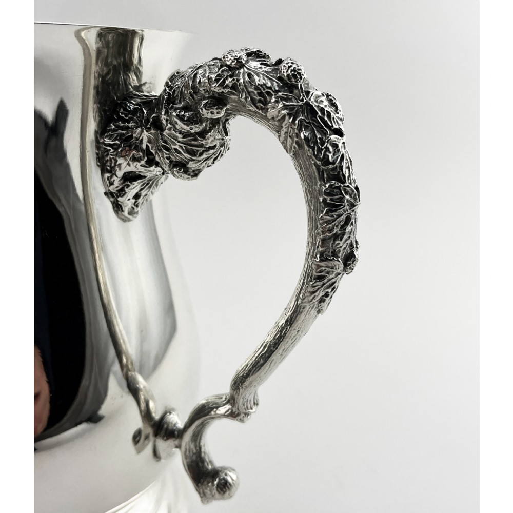 An Edwardian silver-plated loving cup featuring a polished bell-shaped body mounted with three ornate cast handles decorated with vine leaf motifs. View II