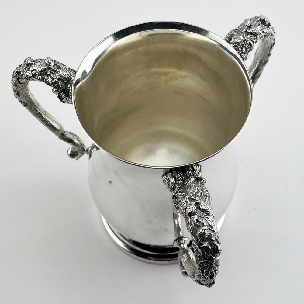 An Edwardian silver-plated loving cup featuring a polished bell-shaped body mounted with three ornate cast handles decorated with vine leaf motifs. View III