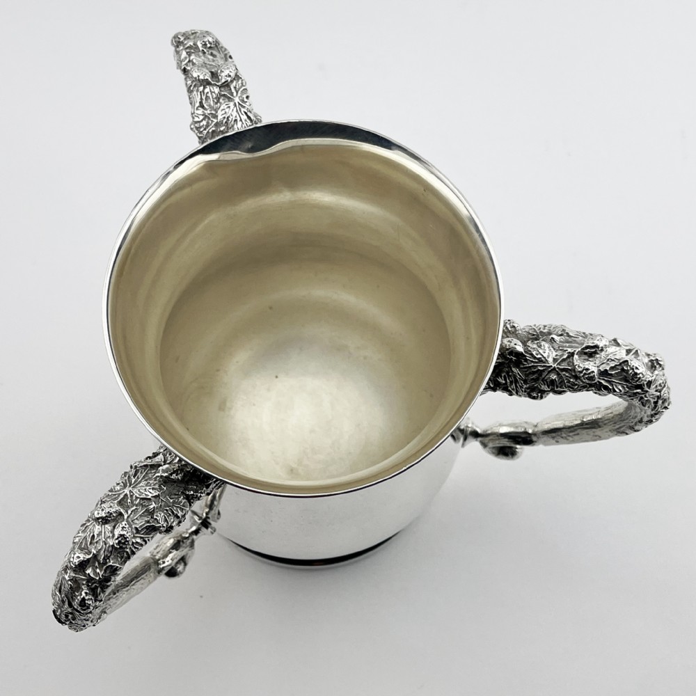 An Edwardian silver-plated loving cup featuring a polished bell-shaped body mounted with three ornate cast handles decorated with vine leaf motifs. View IV