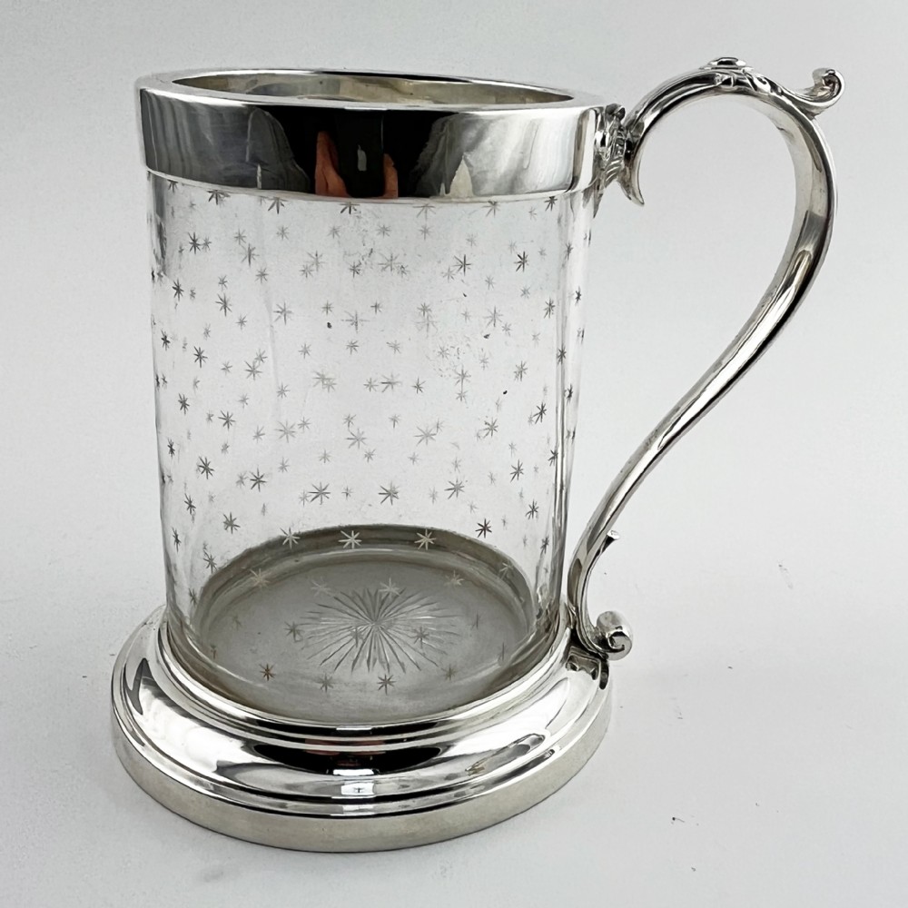 A Victorian clear glass mug featuring etched star motifs, a silver-plated rim, a stepped silver base, and a decorative scrolling handle.