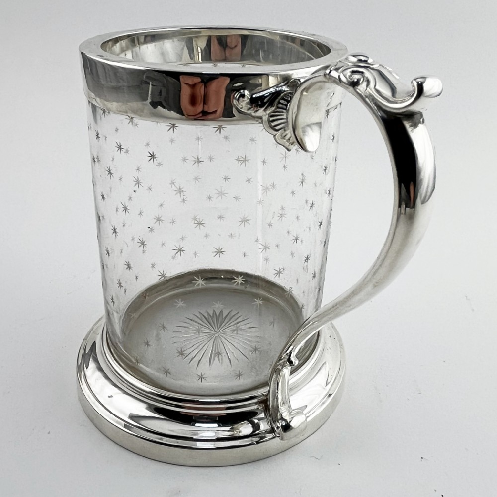 A Victorian clear glass mug featuring etched star motifs, a silver-plated rim, a stepped silver base, and a decorative scrolling handle. View II