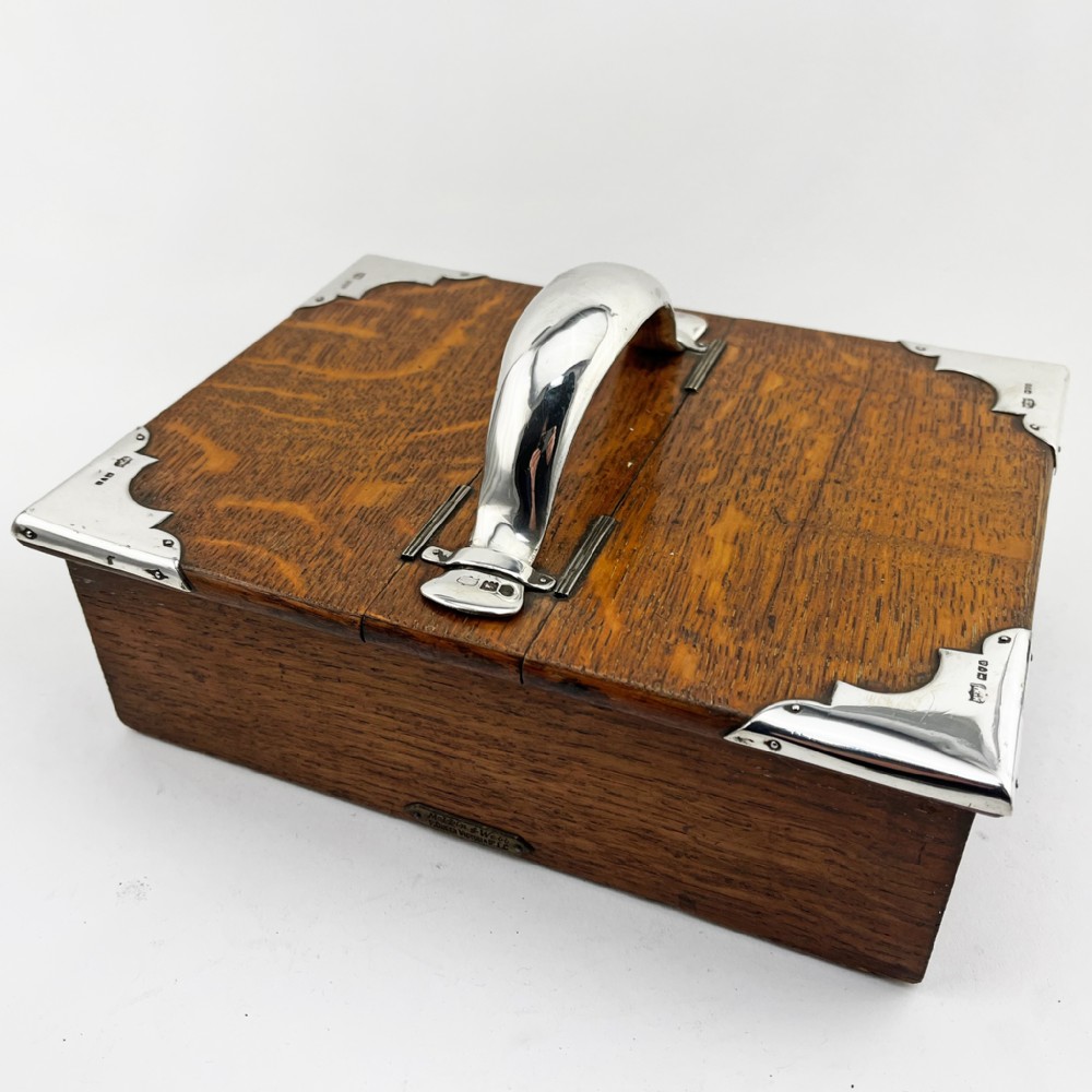 A rectangular oak wood box featuring sterling silver corner mounts and a central silver handle on the lid.