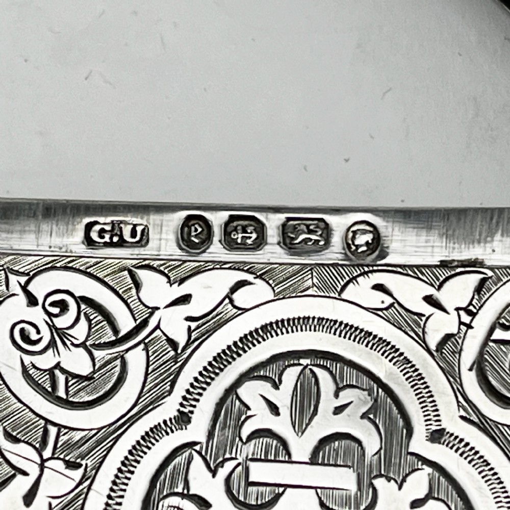 Victorian sterling silver card case featuring intricate foliate hand engraving, scalloped edges, and a central monogrammed cartouche. View V
