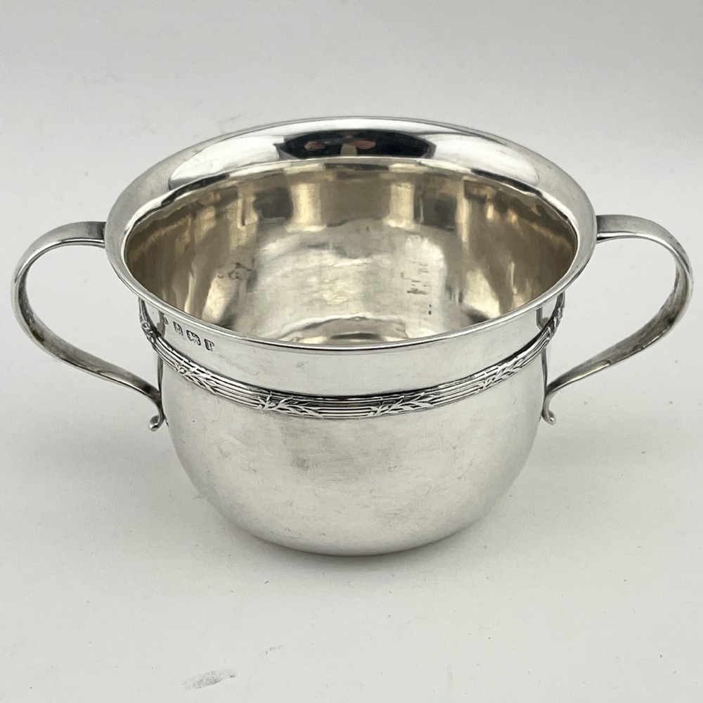 A circular sterling silver porringer featuring two side handles and an engraved decorative band along the rim.