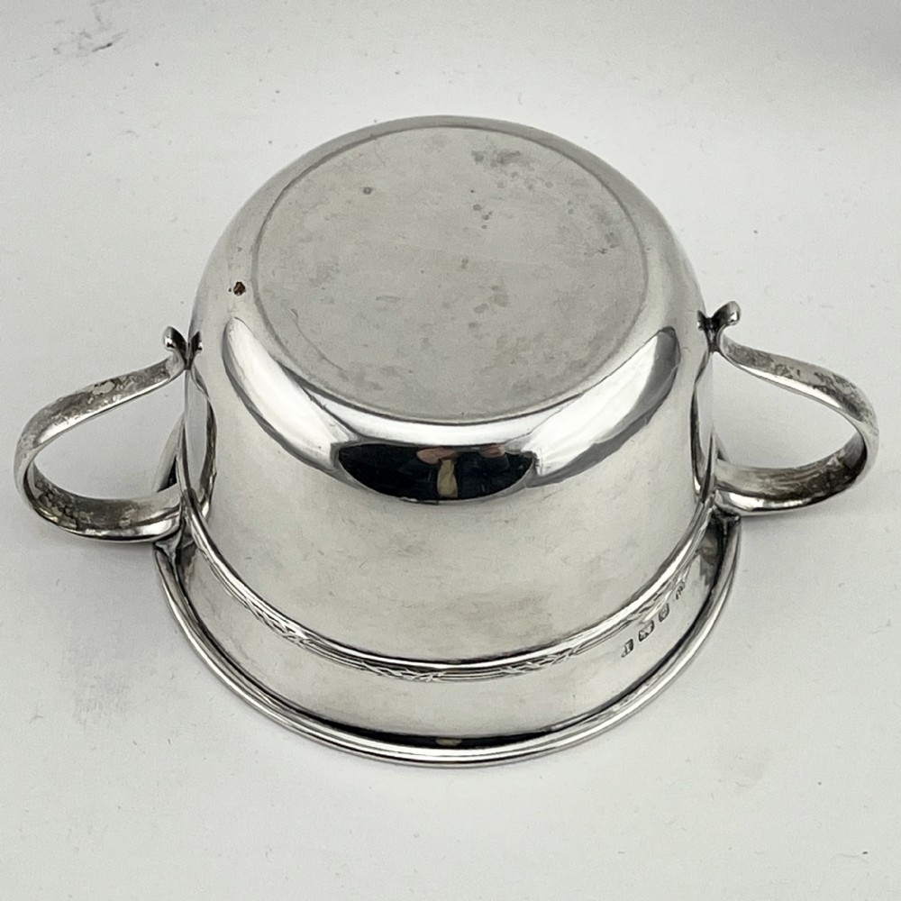A circular sterling silver porringer featuring two side handles and an engraved decorative band along the rim. View V