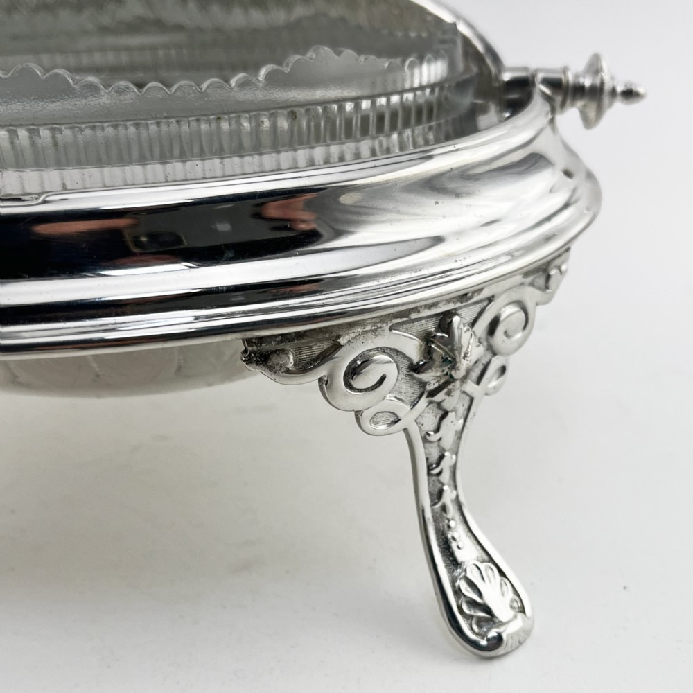 A Victorian silver plated revolving butter dish featuring an engraved domed lid, decorative side pivot handles, and four scrolled legs. View IV