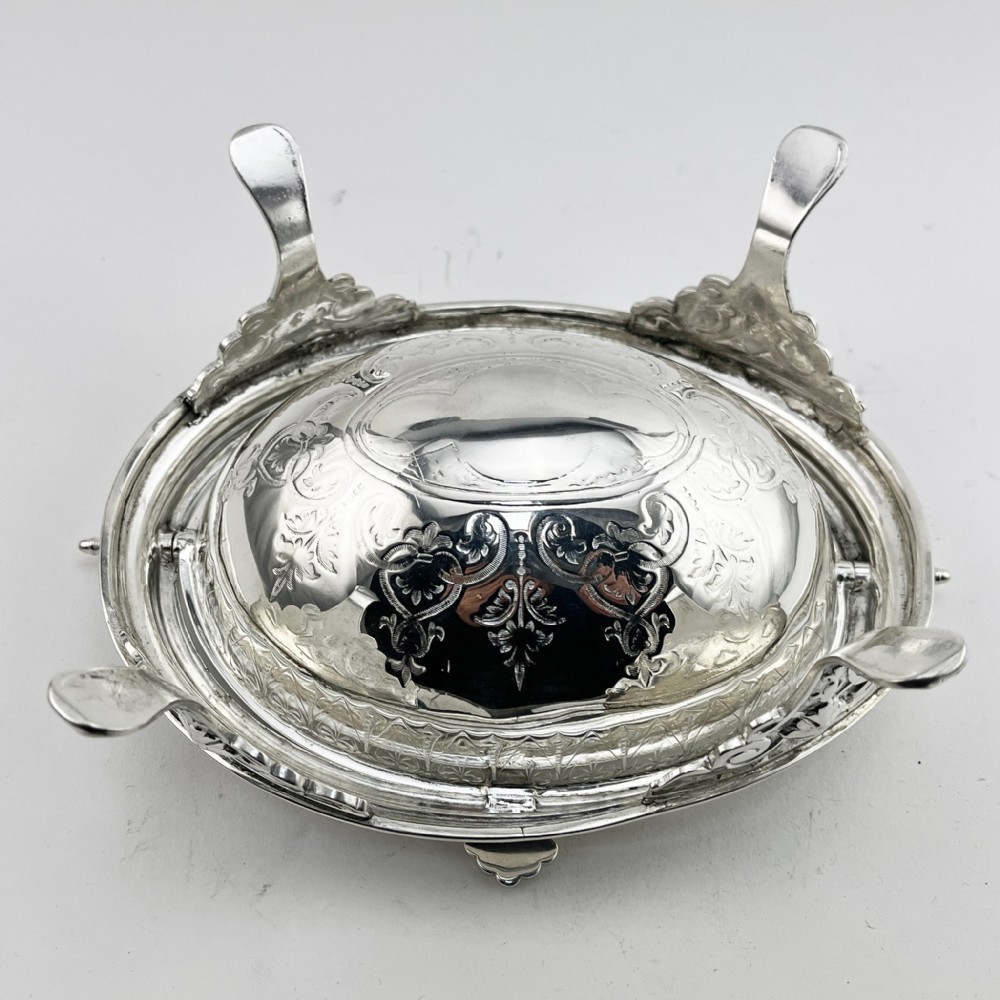 A Victorian silver plated revolving butter dish featuring an engraved domed lid, decorative side pivot handles, and four scrolled legs. View VI