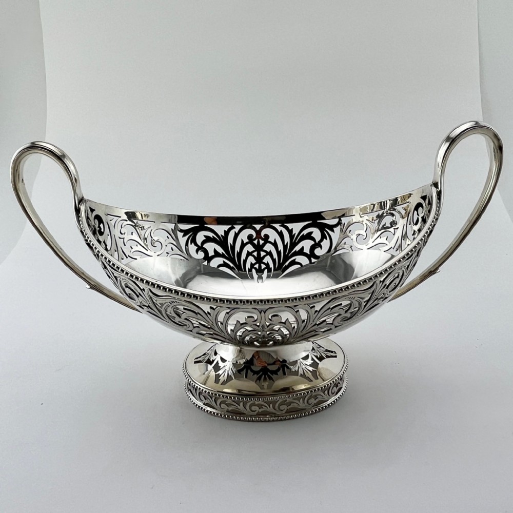 A pair of silver-plated boat-shaped dishes featuring pierced scrollwork borders, high reeded side handles, and oval pedestal bases. View II