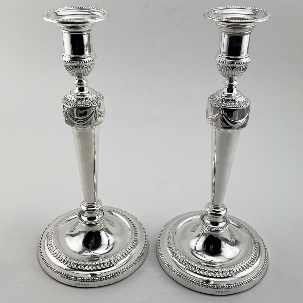 A pair of Victorian silver-plated candlesticks in Georgian Neoclassical style with drapery swags and beaded circular bases.
