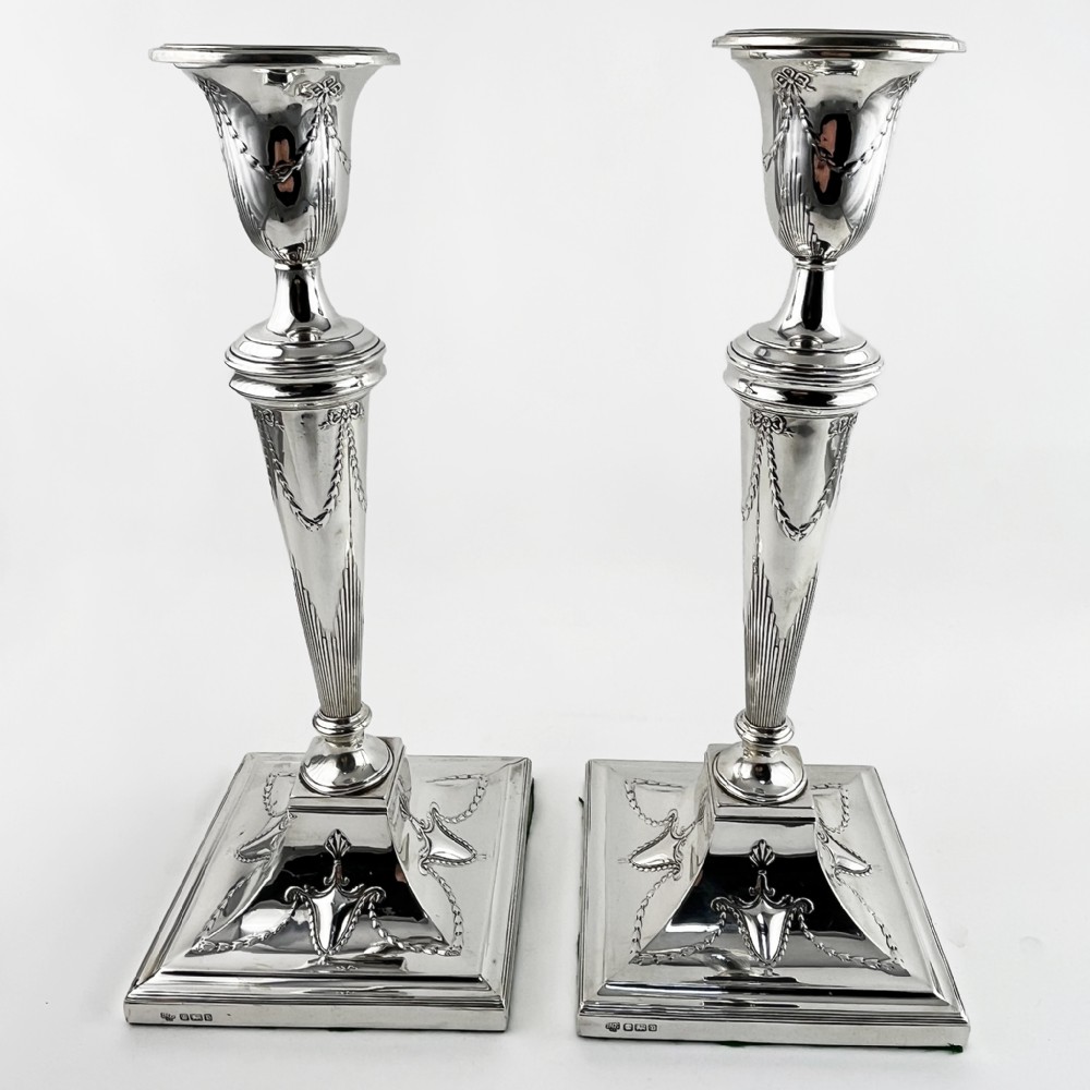 A pair of hallmarked sterling silver candlesticks featuring tapered columns decorated with floral festoons and square stepped bases.