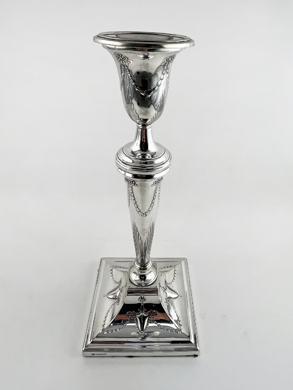 A pair of hallmarked sterling silver candlesticks featuring tapered columns decorated with floral festoons and square stepped bases. View II