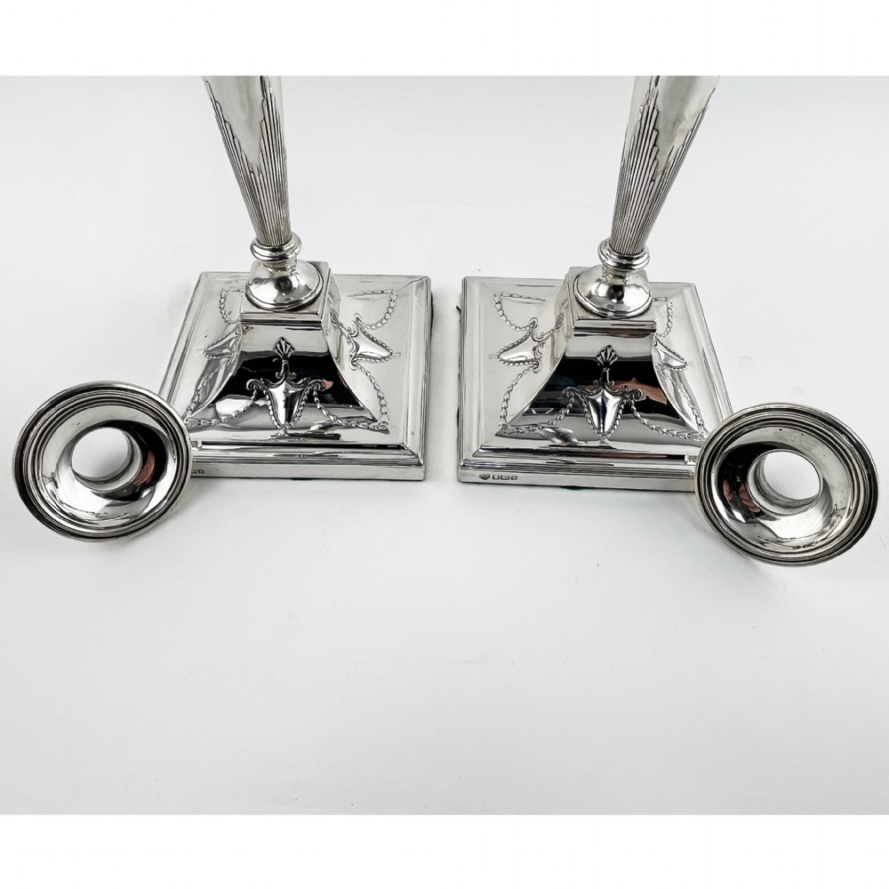 A pair of hallmarked sterling silver candlesticks featuring tapered columns decorated with floral festoons and square stepped bases. View III