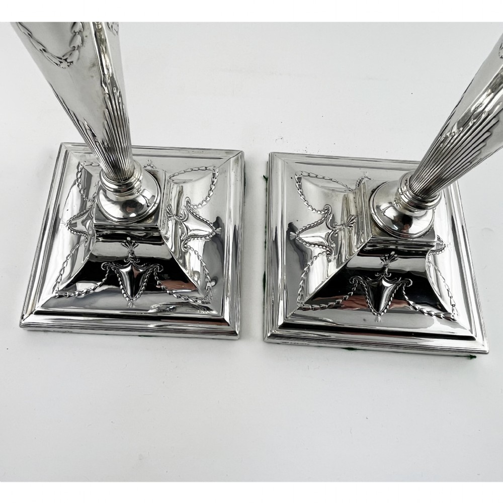 A pair of hallmarked sterling silver candlesticks featuring tapered columns decorated with floral festoons and square stepped bases. View IV