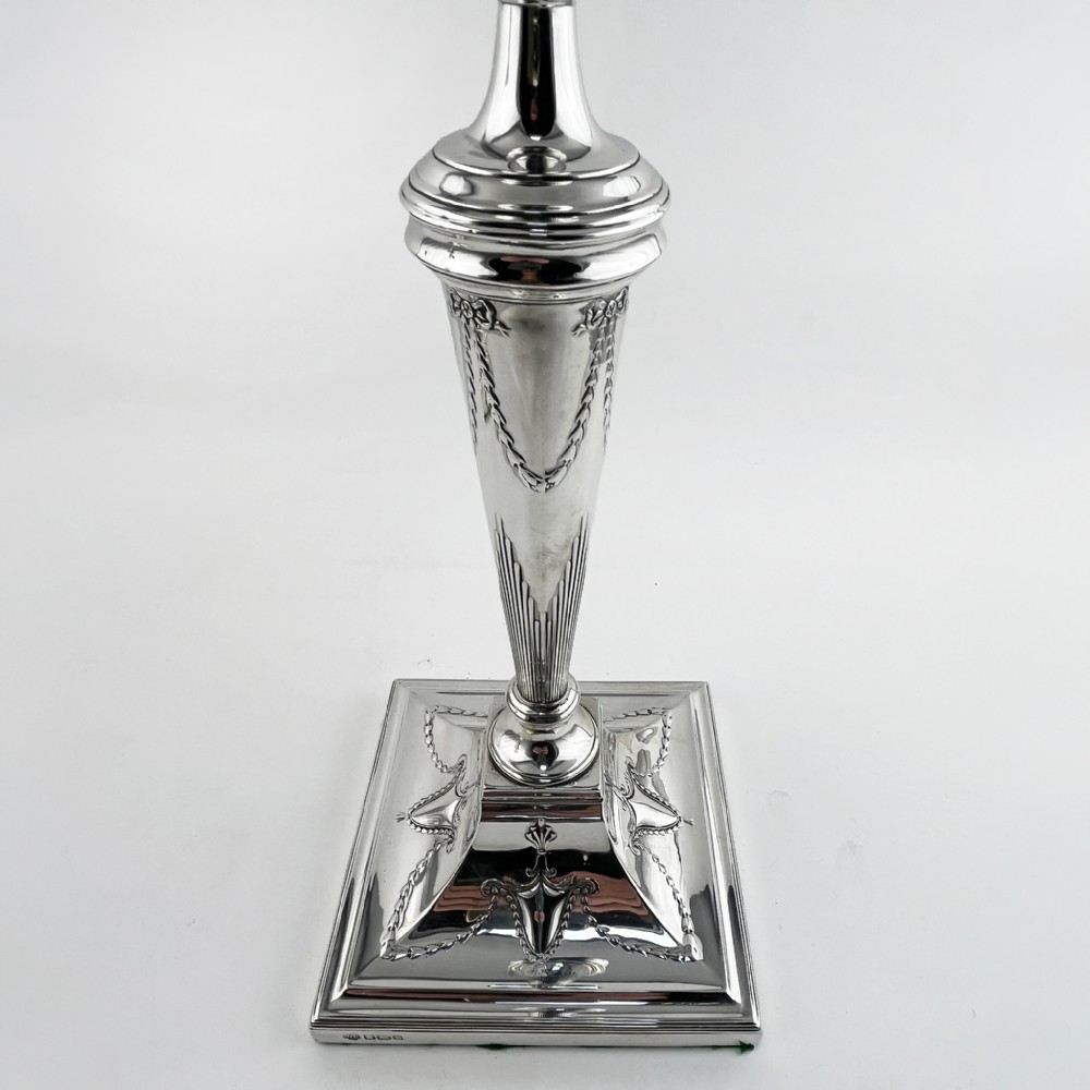 A pair of hallmarked sterling silver candlesticks featuring tapered columns decorated with floral festoons and square stepped bases. View V