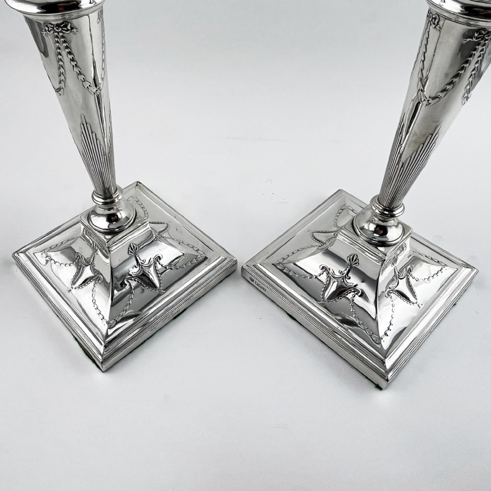 A pair of hallmarked sterling silver candlesticks featuring tapered columns decorated with floral festoons and square stepped bases. View VI