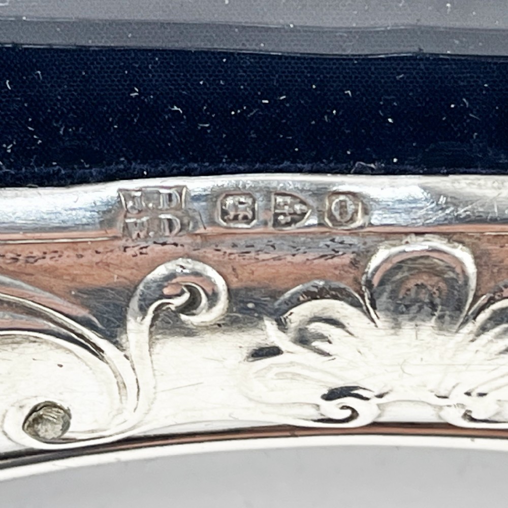 A shaped Victorian sterling silver photograph frame featuring embossed cherub motifs inspired by Reynolds Angels, scrollwork borders, and a dark velvet easel back. View VI