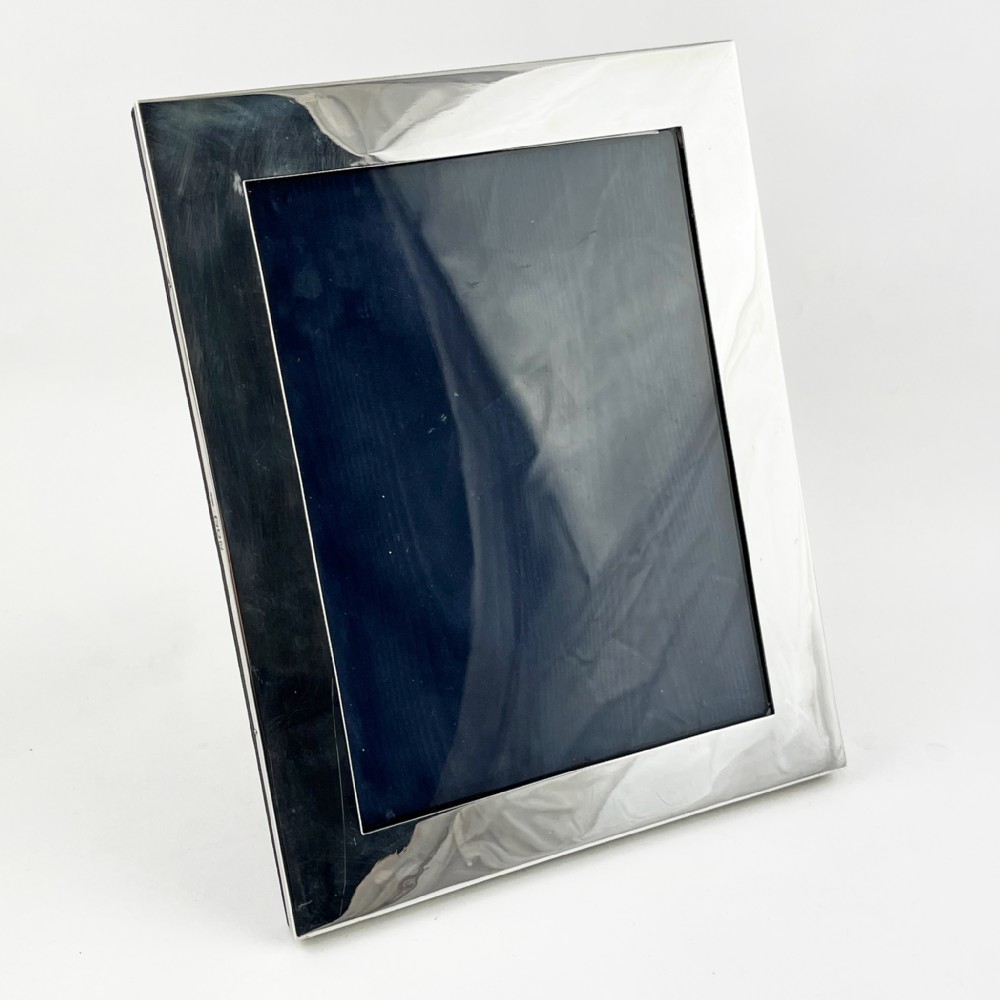 A rectangular sterling silver photo frame with a polished surface, visible hallmarks on the side edge, and a dark backing.