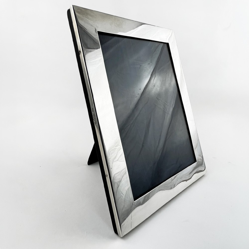 A rectangular sterling silver photo frame with a polished surface, visible hallmarks on the side edge, and a dark backing. View III