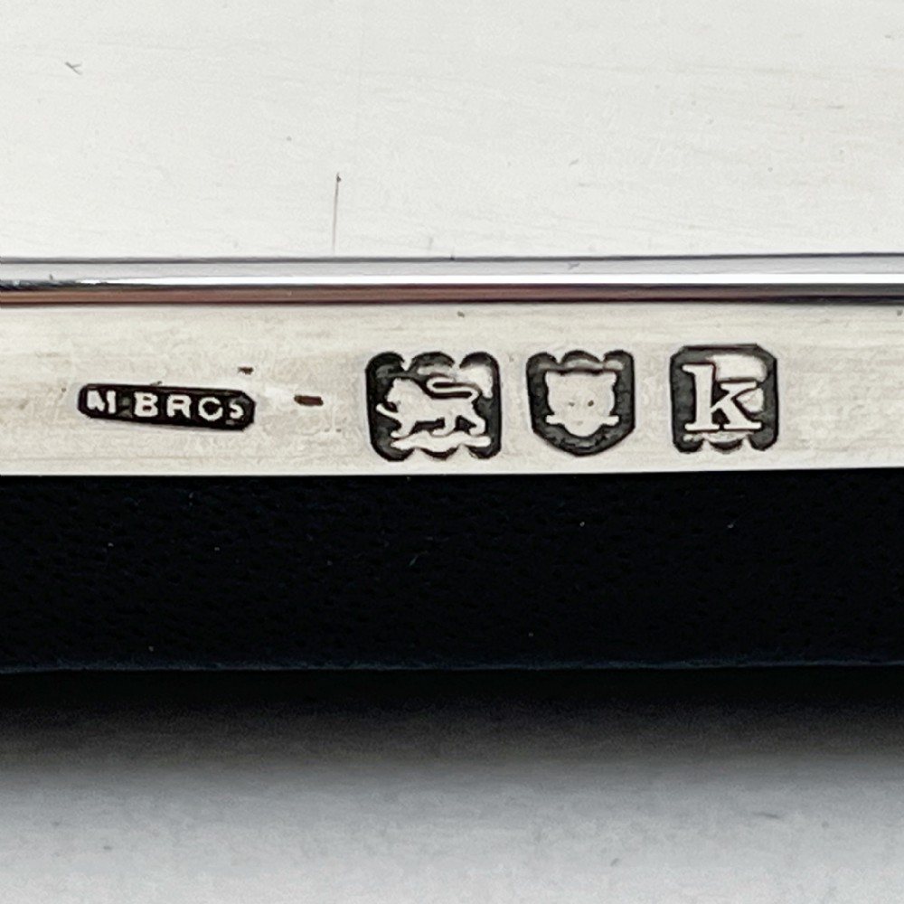A rectangular sterling silver photo frame with a polished surface, visible hallmarks on the side edge, and a dark backing. View V