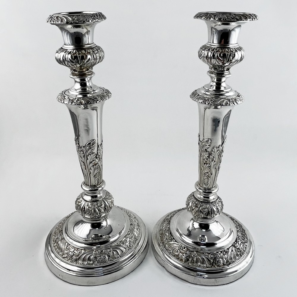 A pair of antique silver-plated candlesticks featuring acanthus leaf motifs, knopped stems, and broad circular bases.
