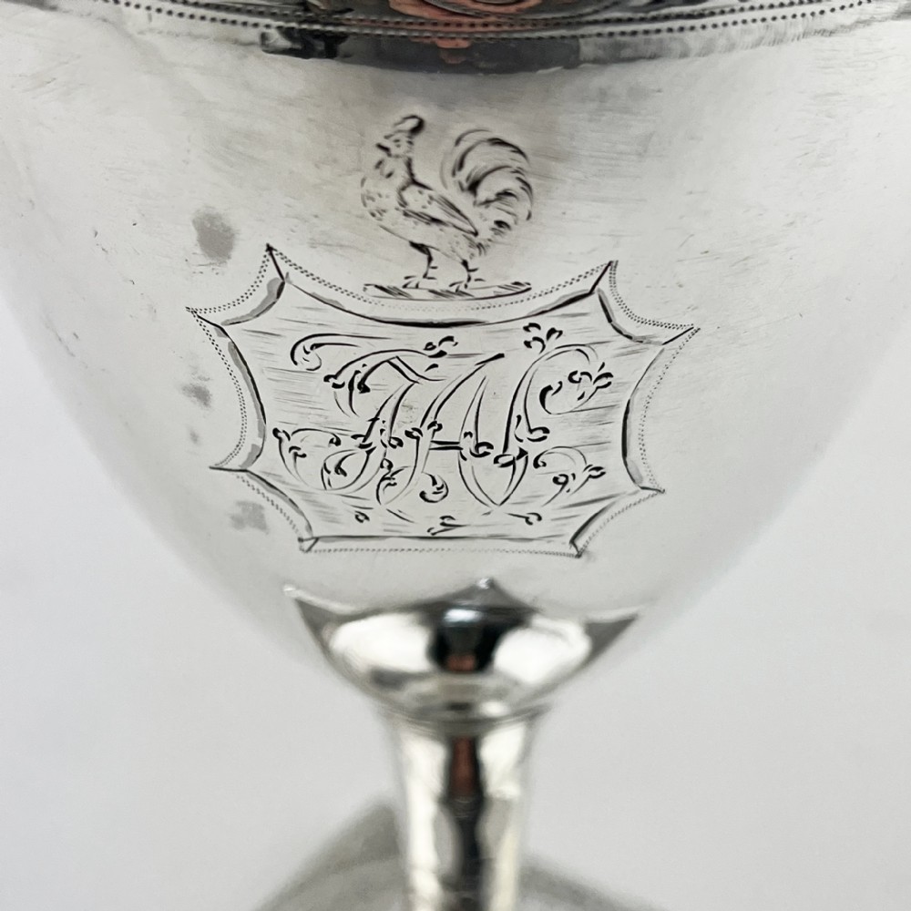 A Georgian sterling silver goblet featuring a vase-shaped bowl with engraved crest and foliate border set upon a square plinth base. View II