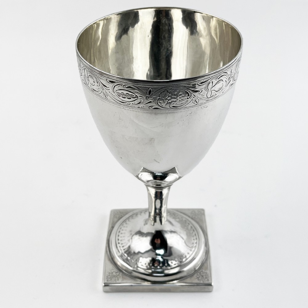 A Georgian sterling silver goblet featuring a vase-shaped bowl with engraved crest and foliate border set upon a square plinth base. View III