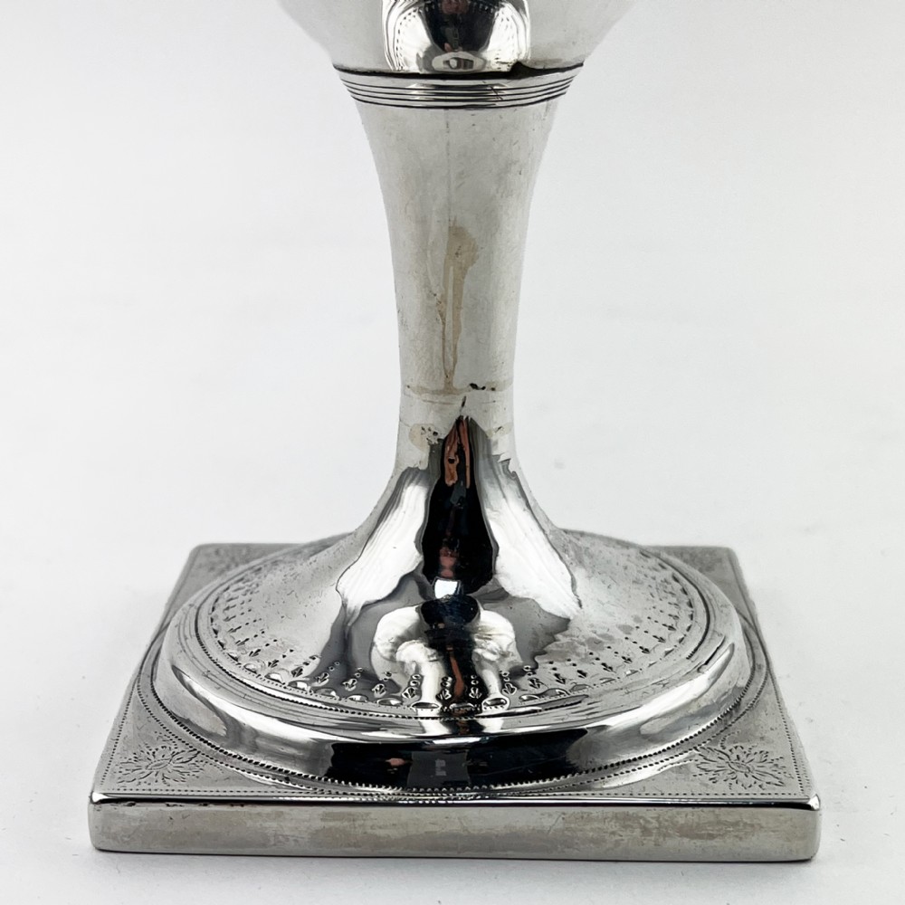 A Georgian sterling silver goblet featuring a vase-shaped bowl with engraved crest and foliate border set upon a square plinth base. View V