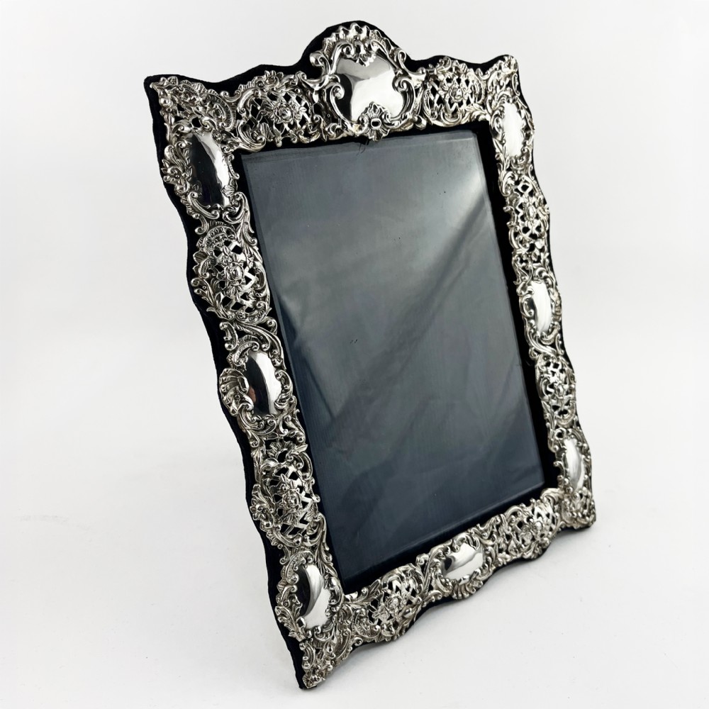 An ornate sterling silver picture frame featuring pierced scrolling foliage and C-scroll motifs backed with dark velvet.