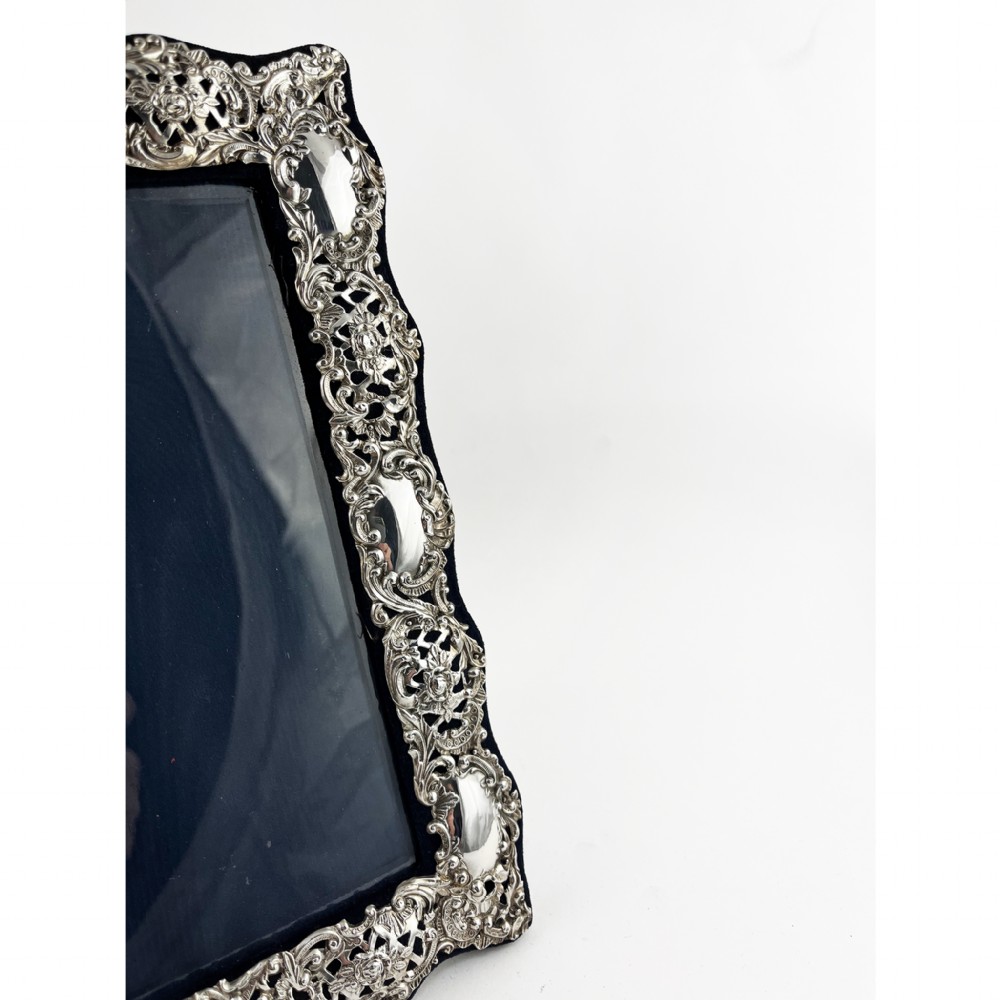 An ornate sterling silver picture frame featuring pierced scrolling foliage and C-scroll motifs backed with dark velvet. View II