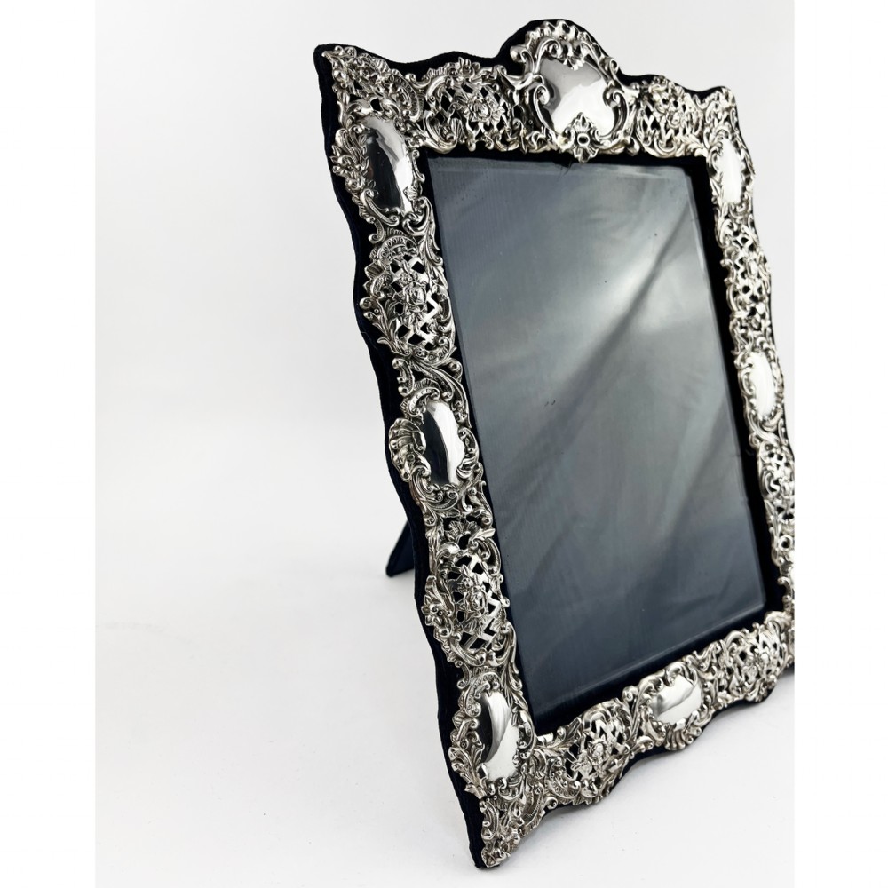 An ornate sterling silver picture frame featuring pierced scrolling foliage and C-scroll motifs backed with dark velvet. View III