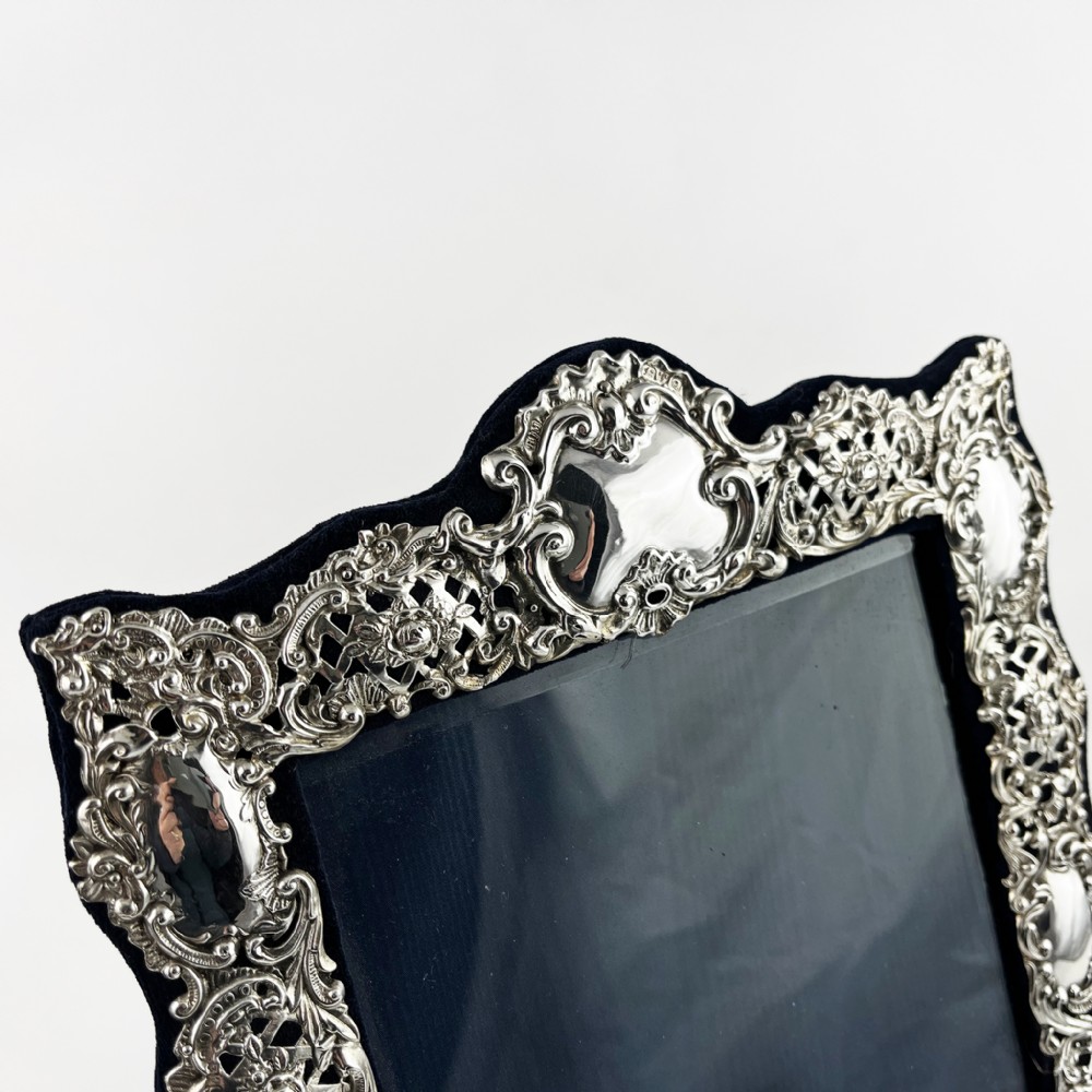 An ornate sterling silver picture frame featuring pierced scrolling foliage and C-scroll motifs backed with dark velvet. View IV