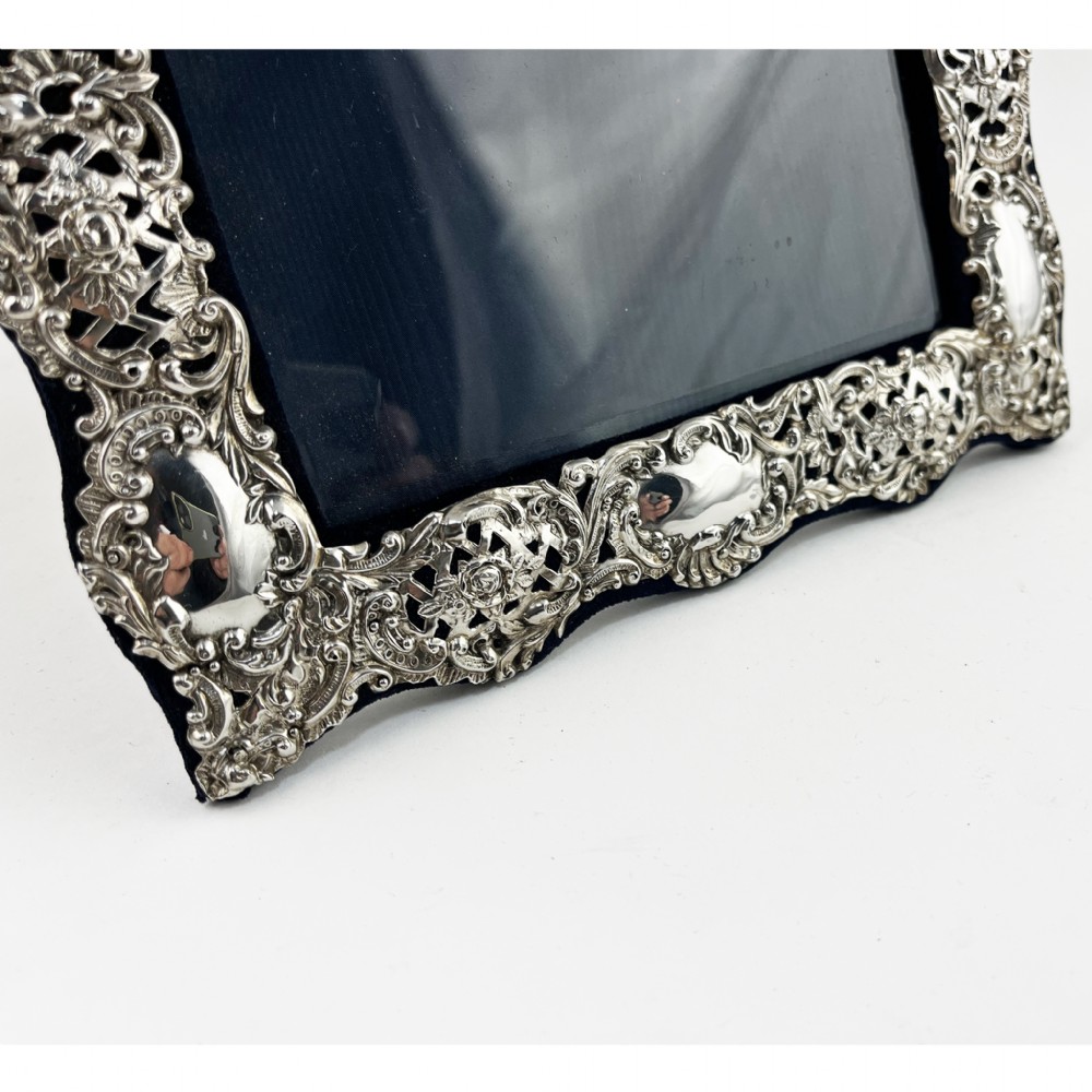 An ornate sterling silver picture frame featuring pierced scrolling foliage and C-scroll motifs backed with dark velvet. View V