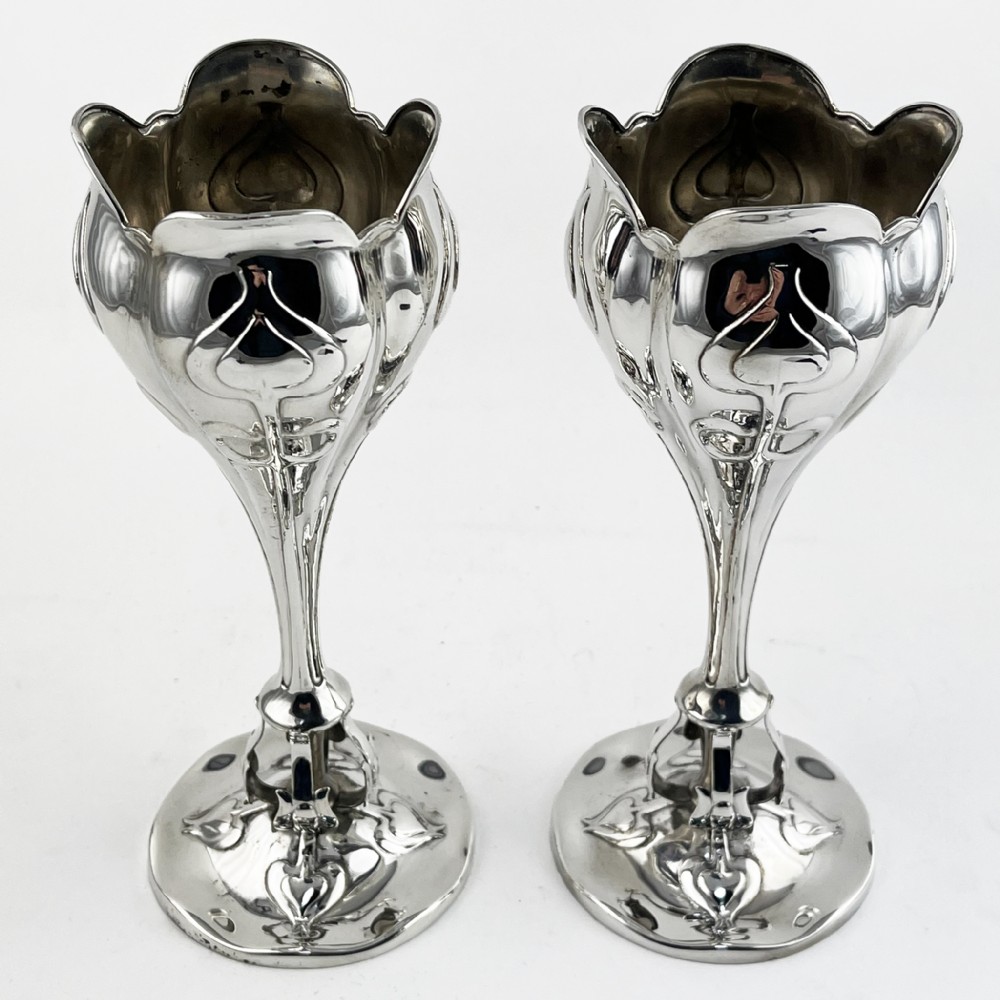 A pair of polished sterling silver Art Nouveau stem vases featuring flared scalloped rims, slender stems, and embossed floral whiplash motifs on circular bases.