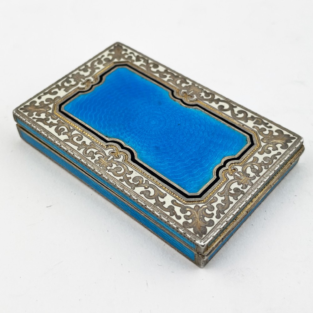 A rectangular sterling silver card case featuring bright blue guilloche enamel framed by white scroll enamel and silver gilt borders.