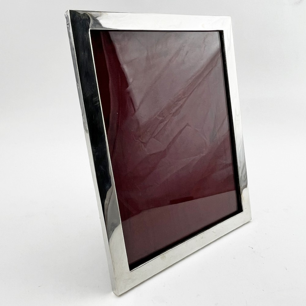 A rectangular sterling silver photo frame with a polished plain border standing vertically on an easel back.