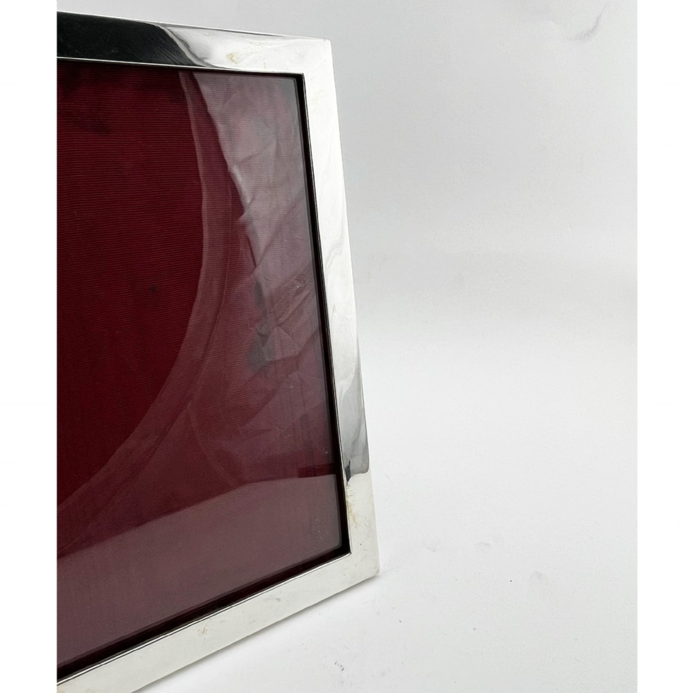A rectangular sterling silver photo frame with a polished plain border standing vertically on an easel back. View II
